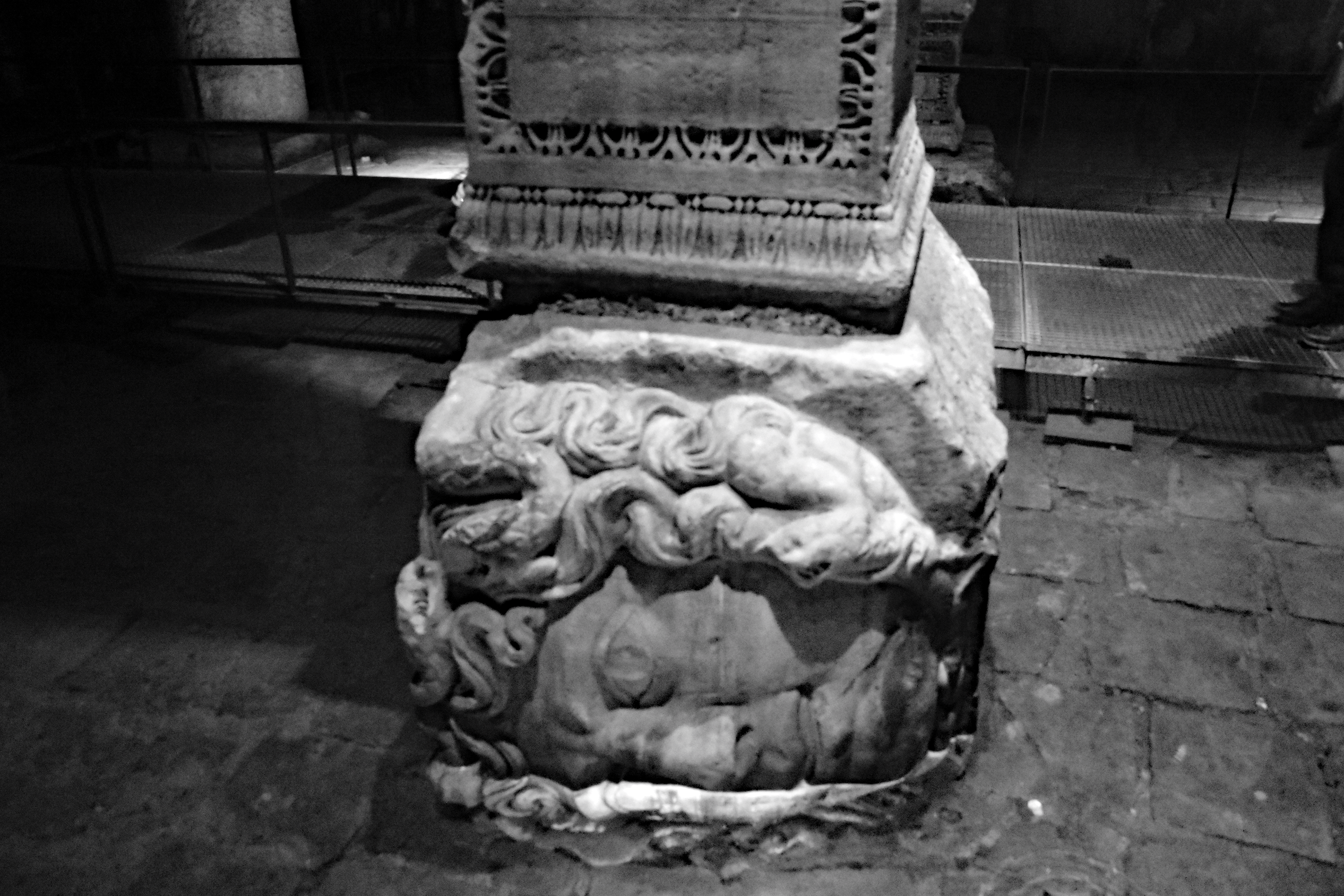 Close-up view of a carved marble base with intricate details featuring figures and serpents, located in the Basilica Cisterns of Istanbul.