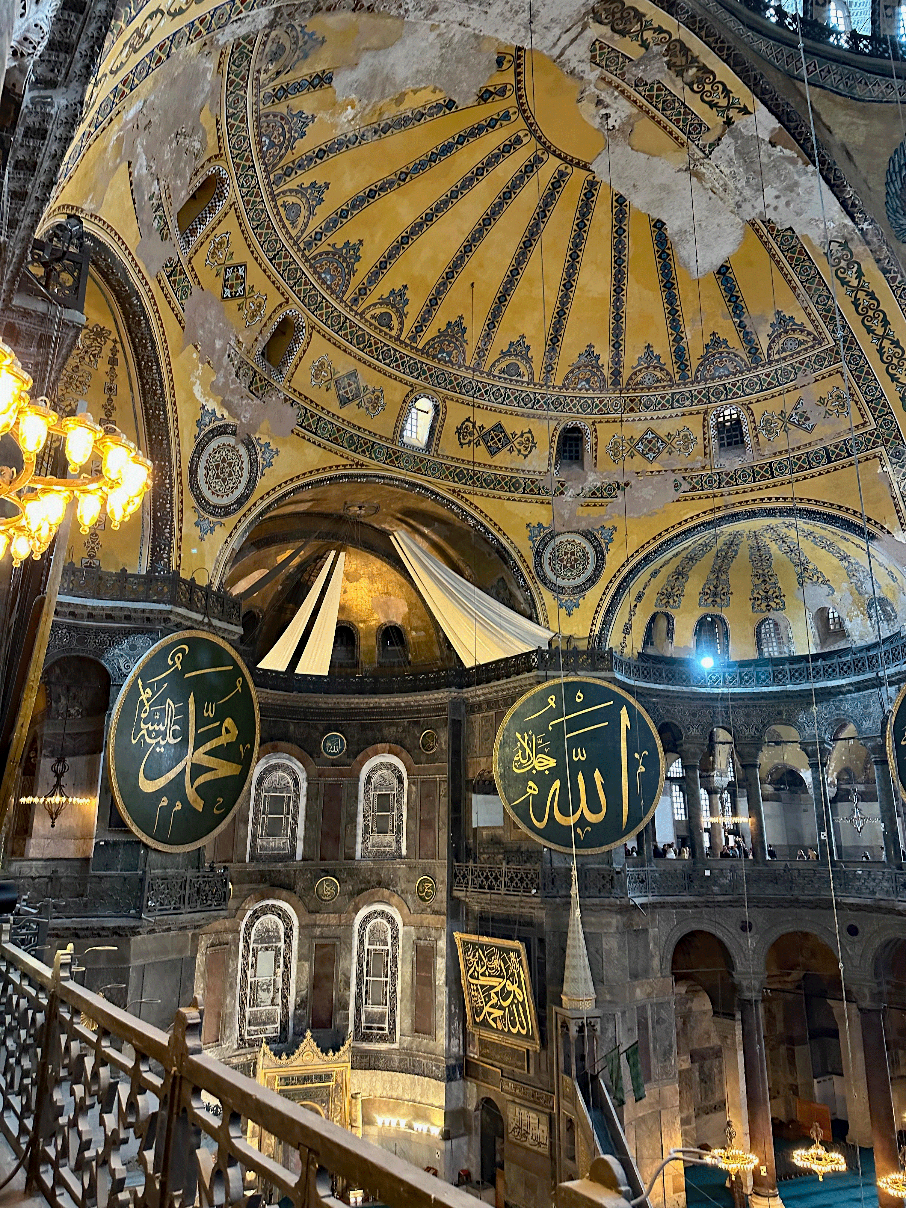 Interior view of Hagia Sophia showcasing its intricate dome, decorative patterns, and large Arabic calligraphy signs on the walls.
