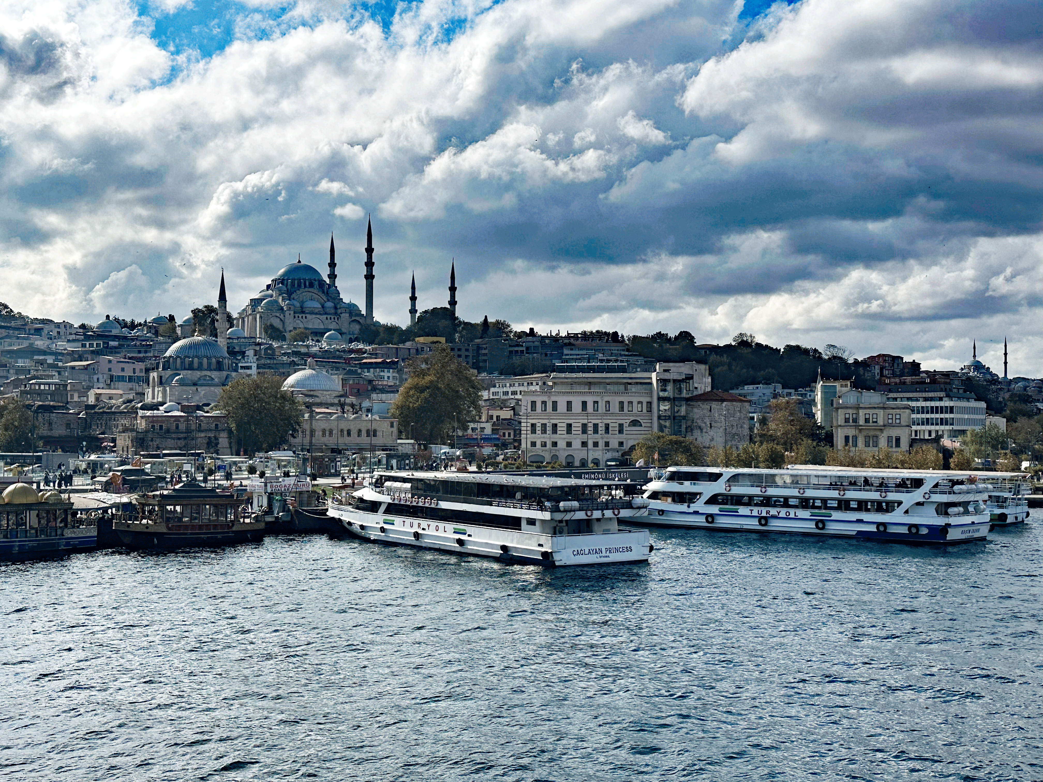 A scenic view of Istanbul's skyline featuring the domes and minarets of historic mosques and boats docked along the waterfront.