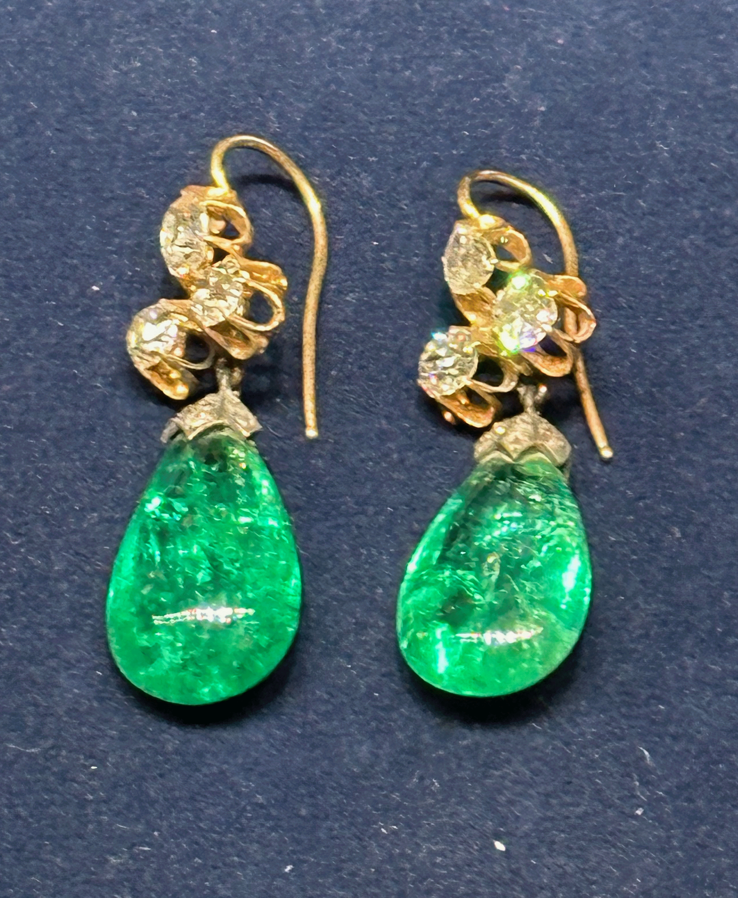 A pair of vintage earrings featuring gold hooks and intricate designs with sparkling clear stones, complemented by vibrant green teardrop-shaped gems.