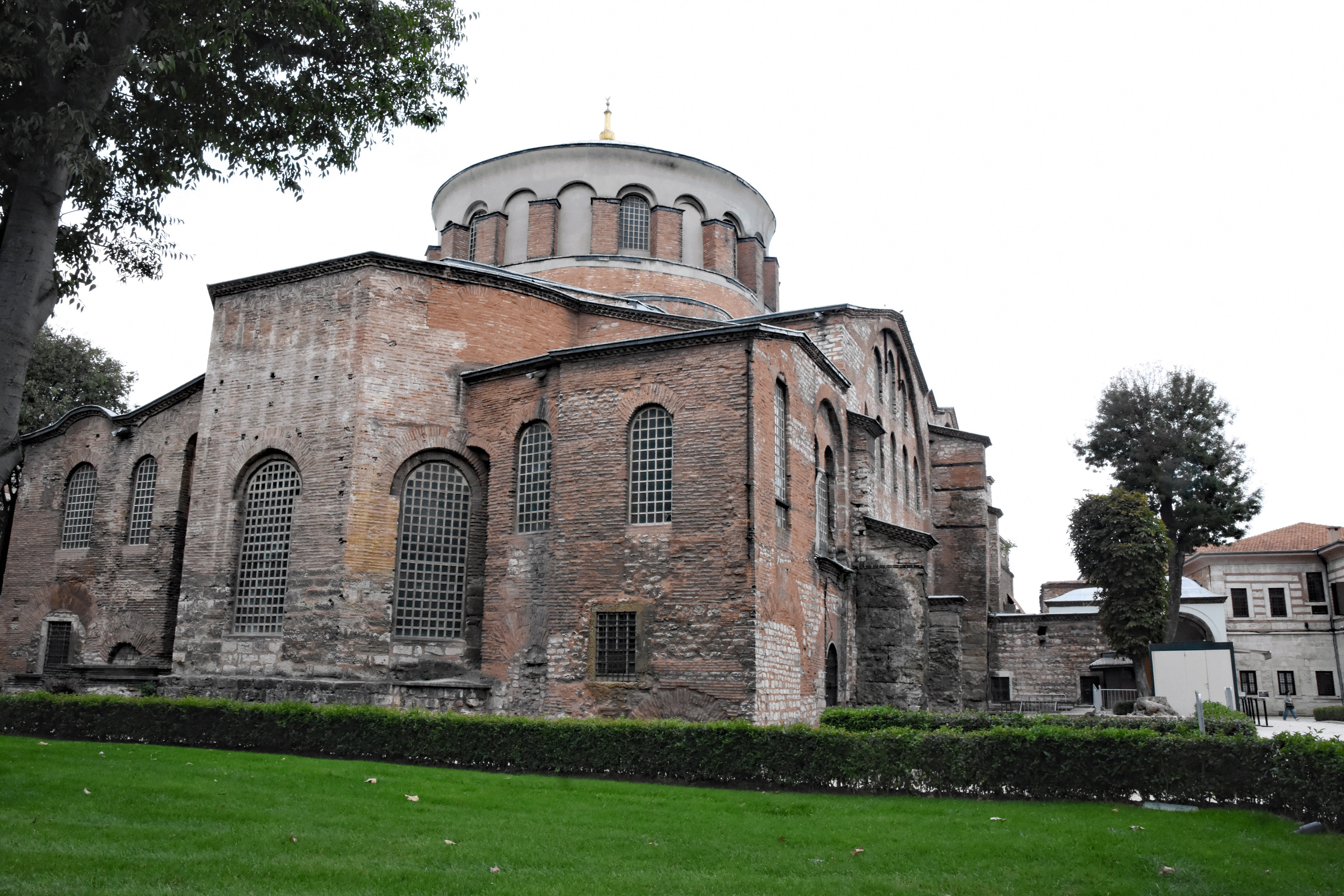 Side view of the Hagia Sophia, showcasing its distinct architectural features, including the rounded dome and brick facade, surrounded by greenery.