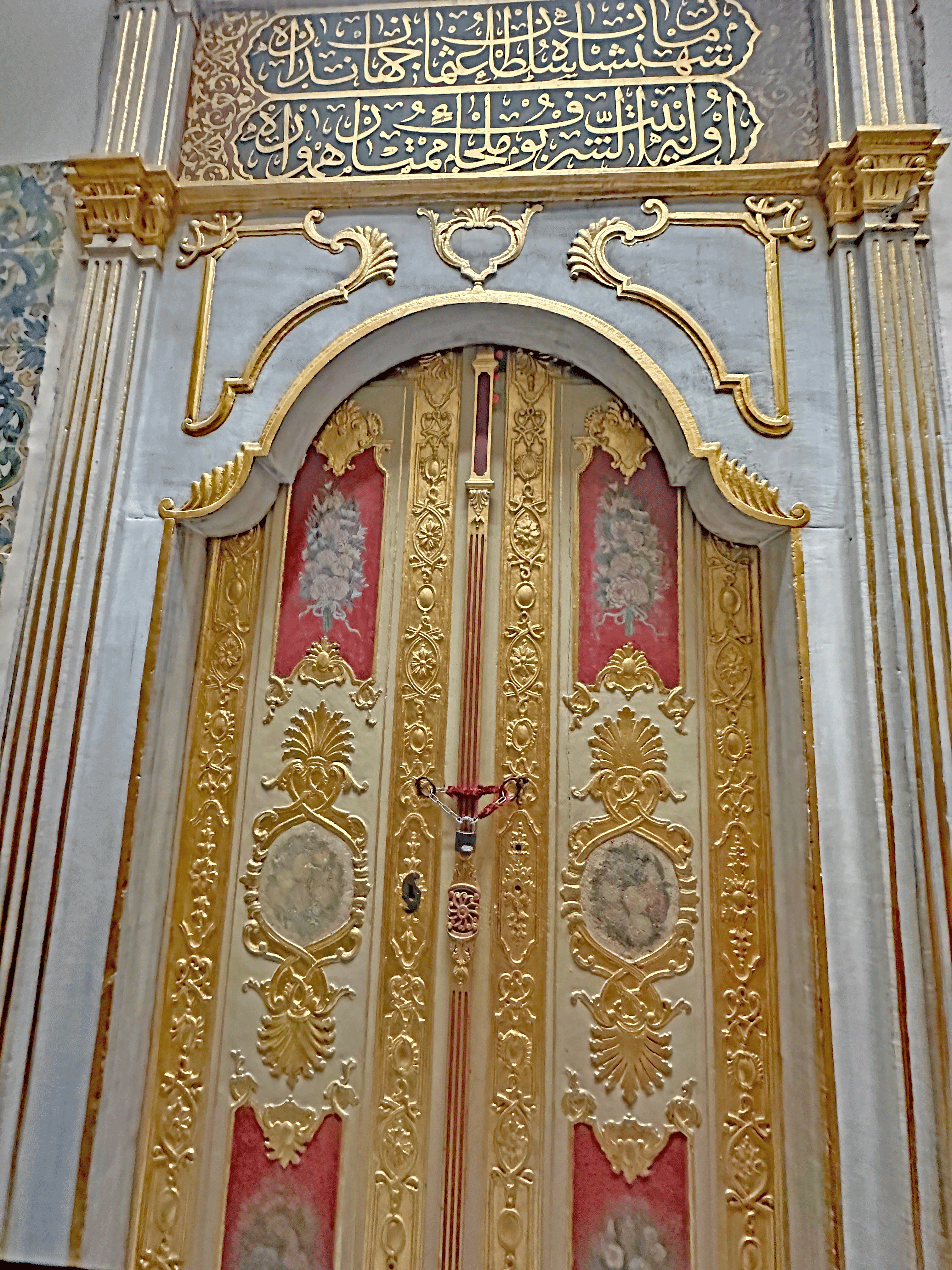 Ornate golden doors with intricate designs and decorative elements, complemented by ornate inscriptions above.