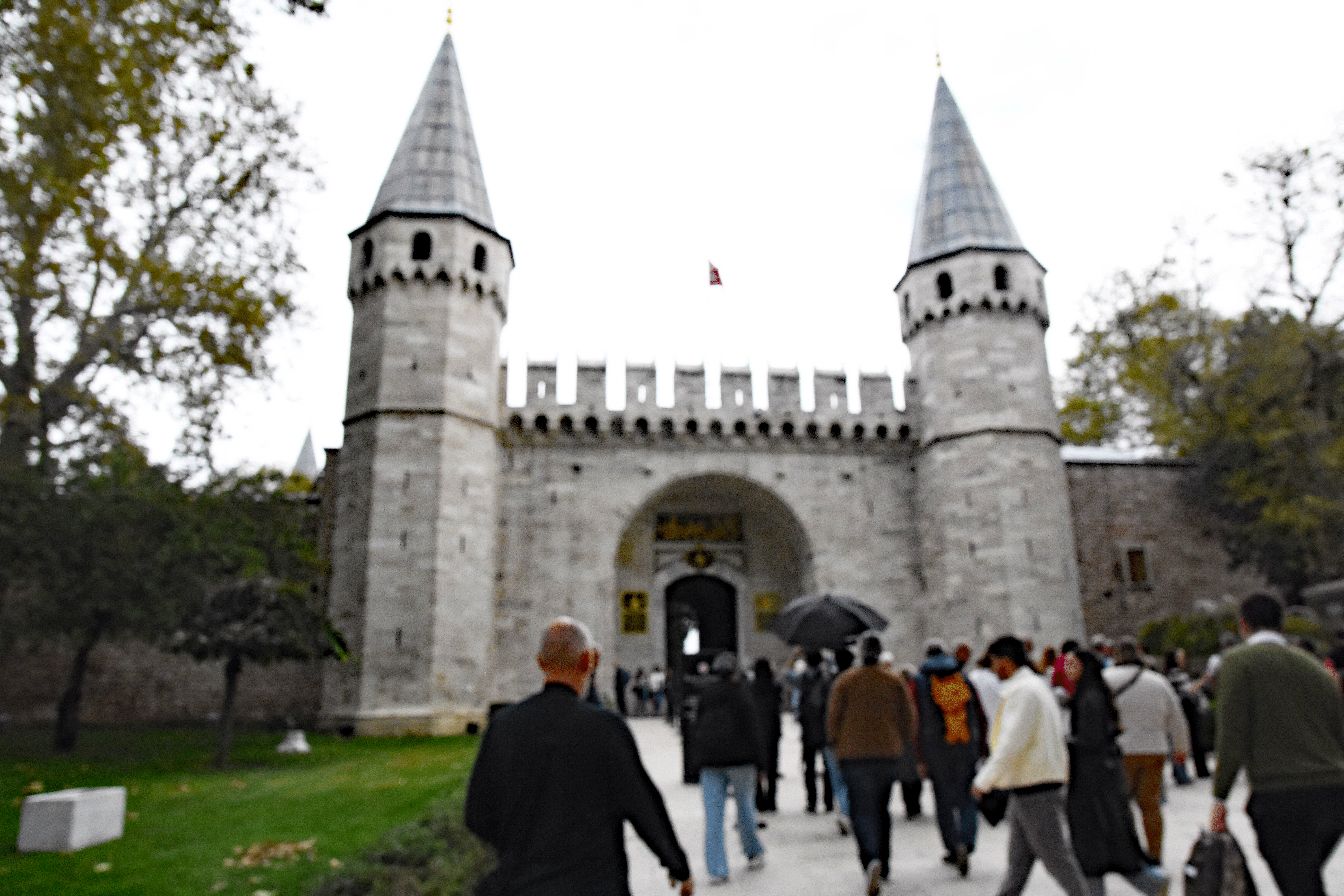 Visitors approaching the grand entrance of Topkapi Palace in Istanbul, showcasing its historic architecture with two tall towers and a bustling crowd.