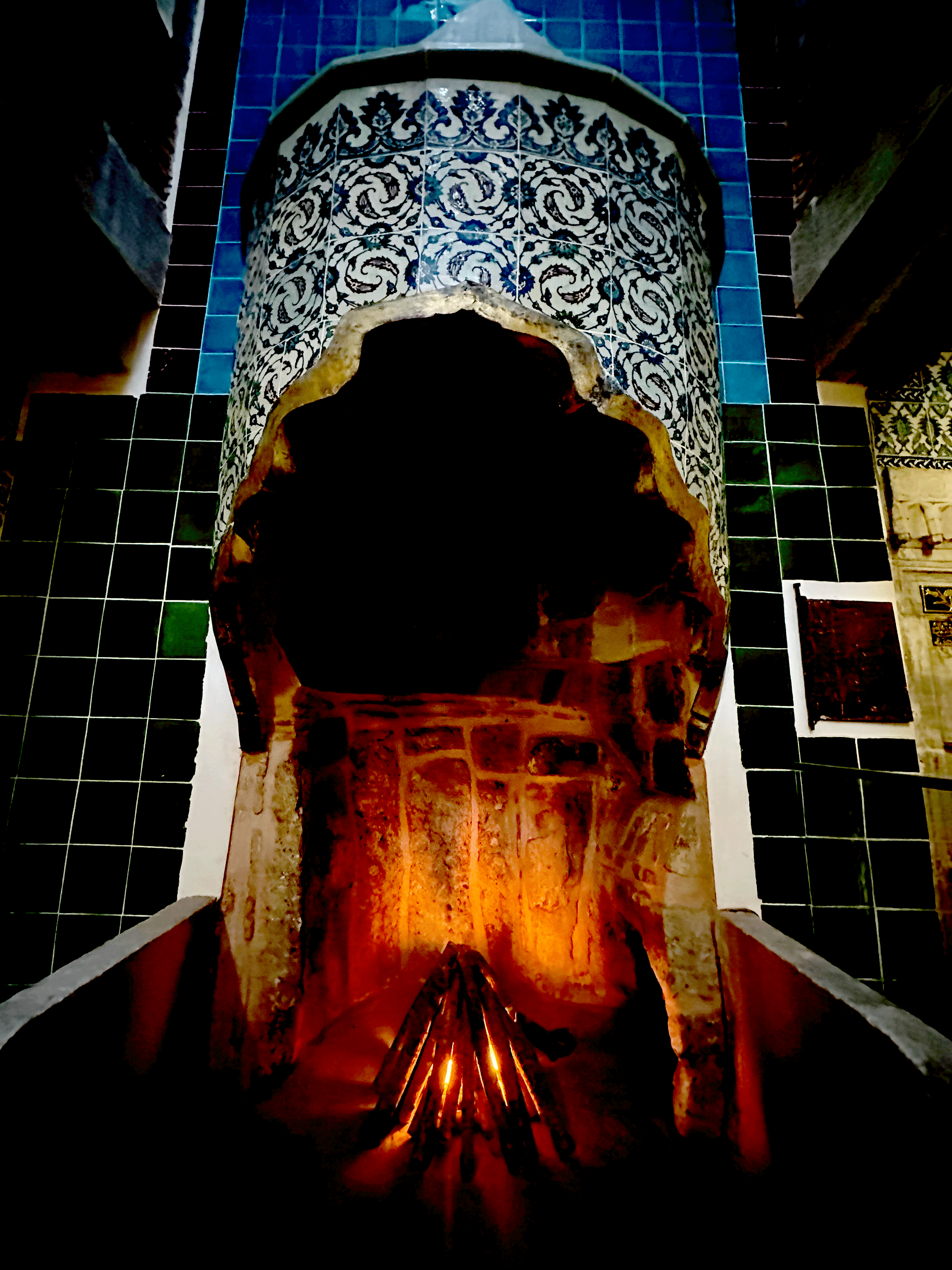 Interior view of a traditional Turkish bath, featuring intricately tiled walls and a small firepit in the center.
