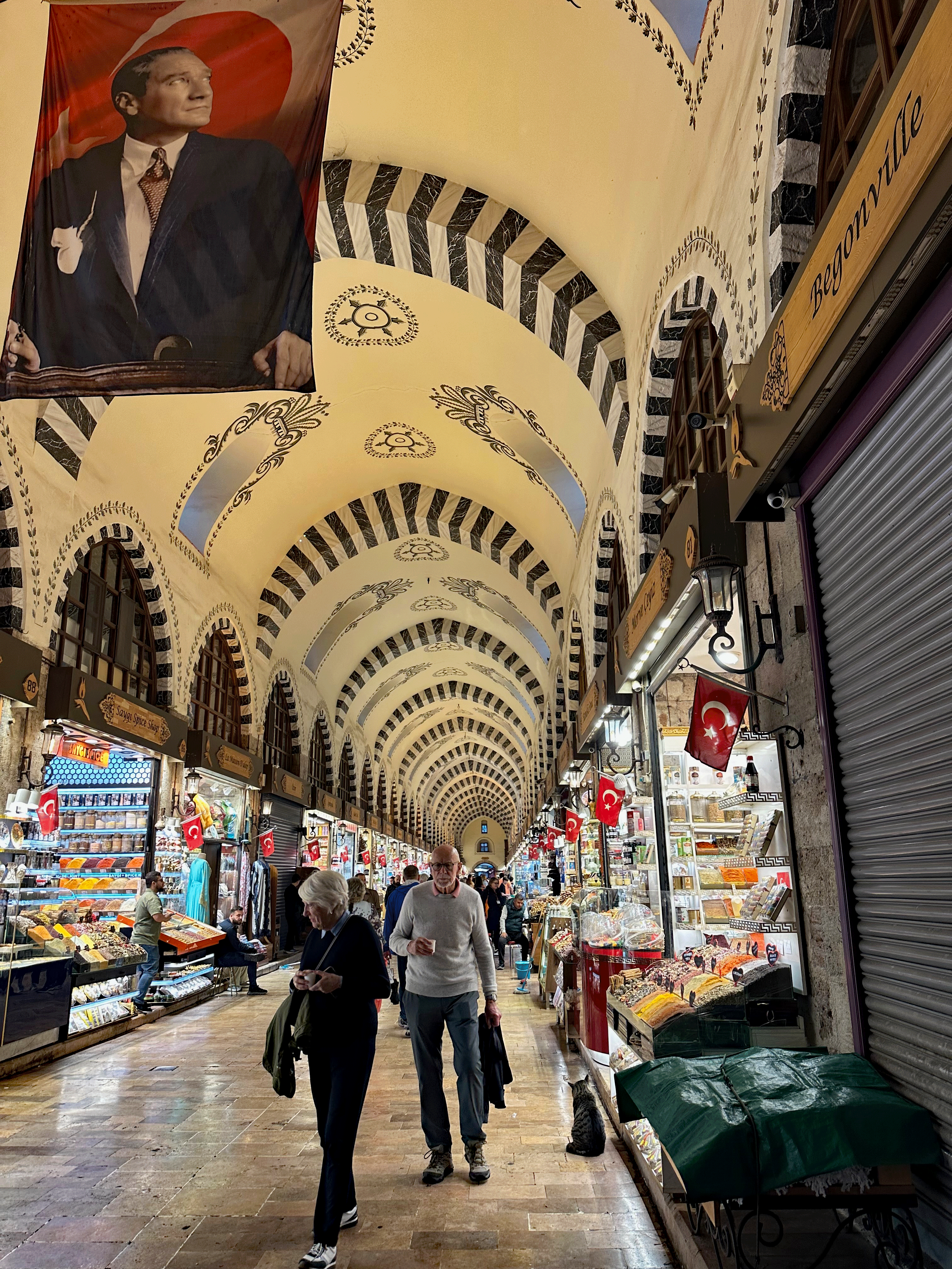 Interior view of the Spice Market in Istanbul, showcasing a bustling atmosphere with shoppers browsing a variety of goods, colorful displays of spices and sweets, and decorative arches above.