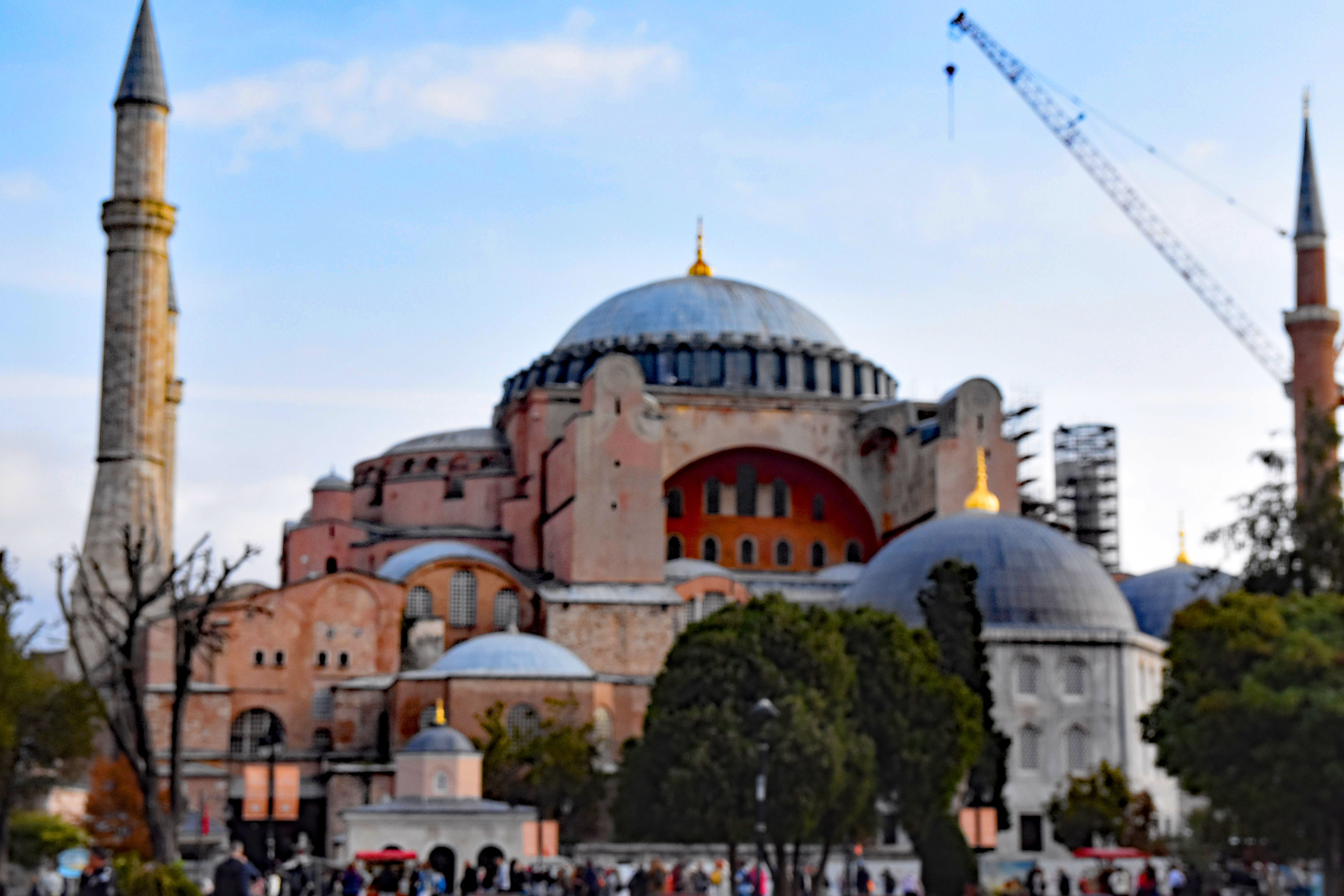 A view of the Hagia Sophia in Istanbul, showcasing its distinct domes and minarets, set against a partly cloudy sky with a construction crane visible in the background.