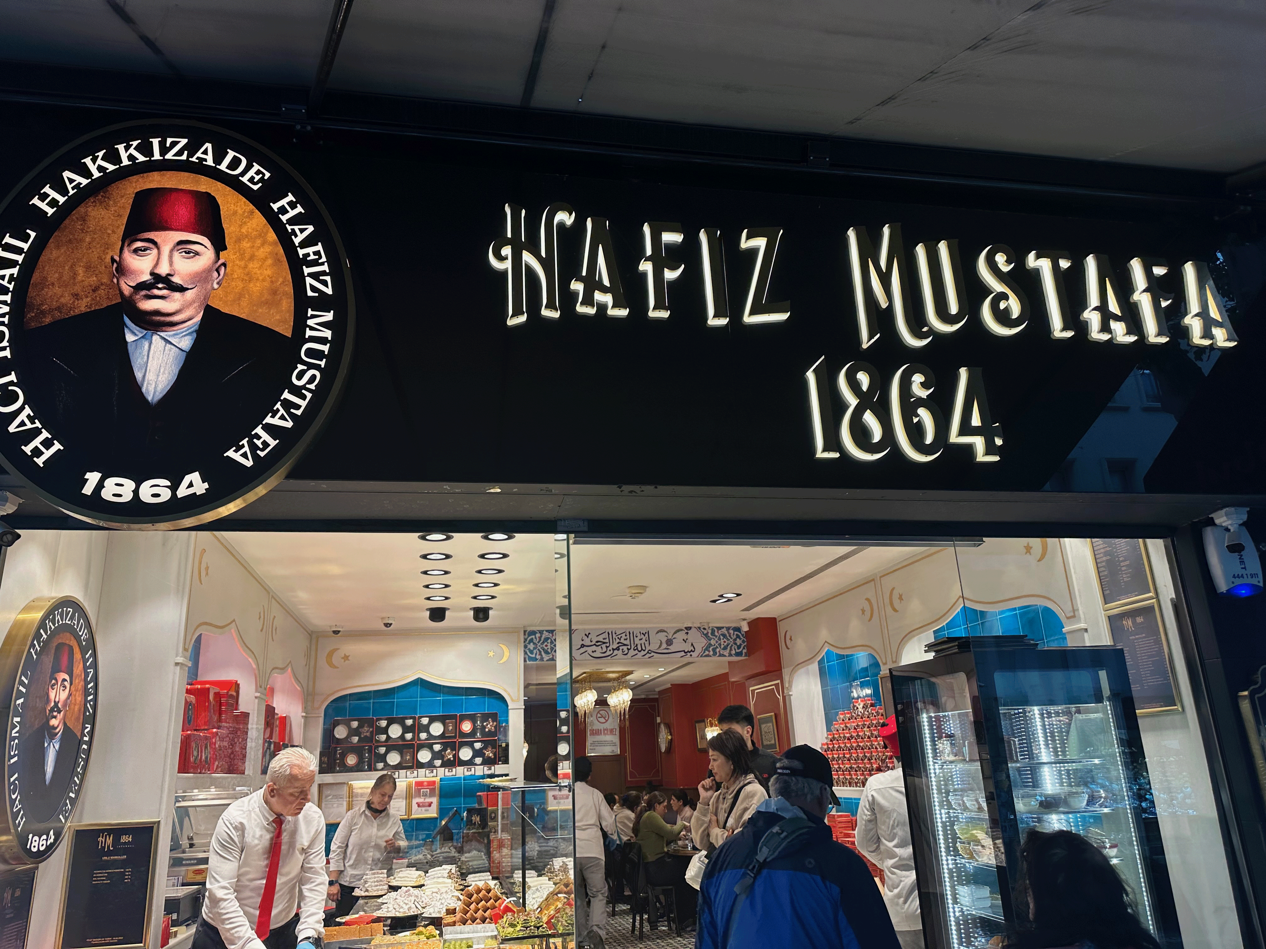 Exterior view of Hafiz Mustafa, a renowned Turkish dessert shop established in 1864, showcasing a welcoming atmosphere with customers inside.