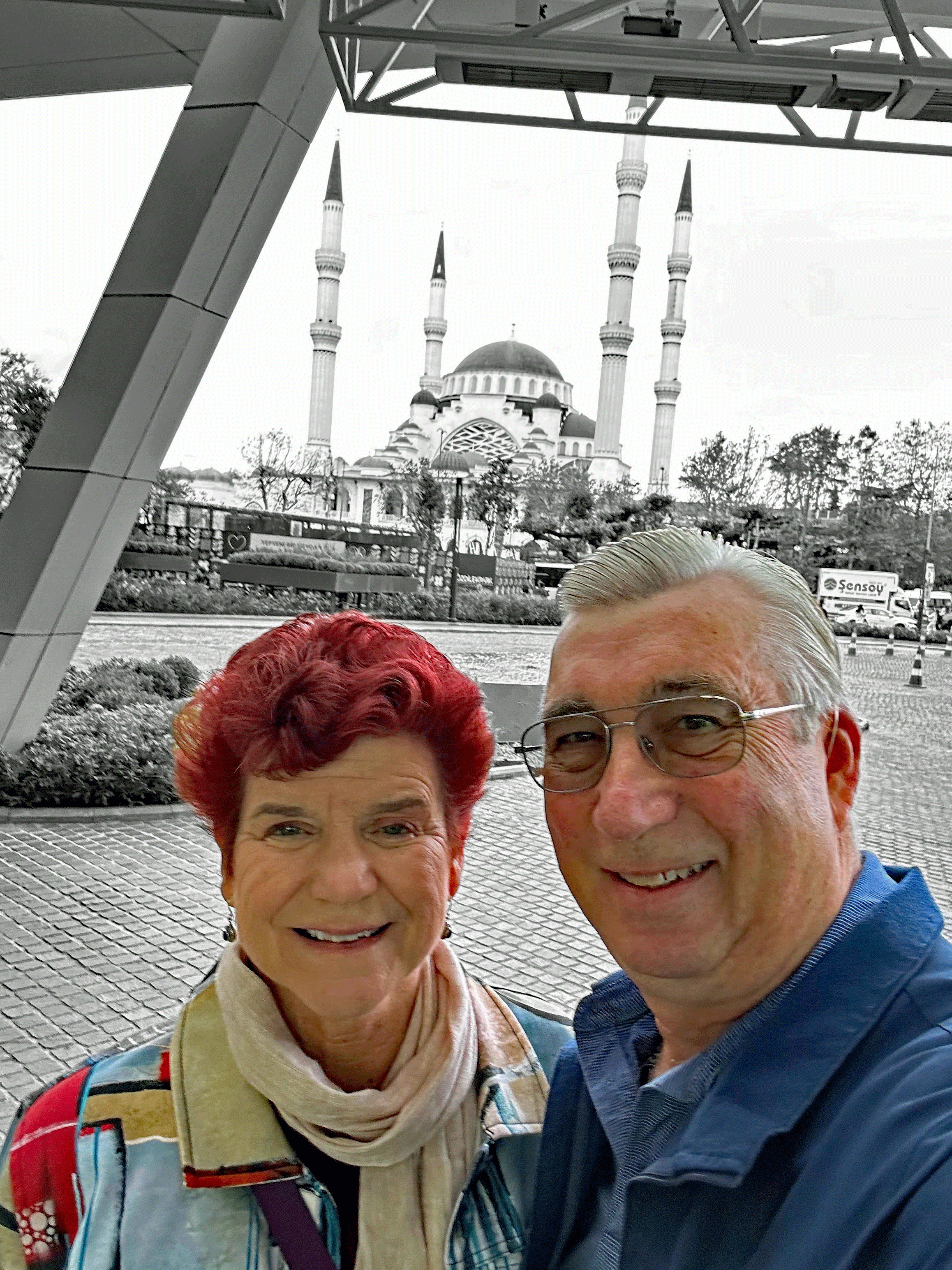 A couple poses for a selfie with a mosque featuring multiple minarets in the background in Istanbul.